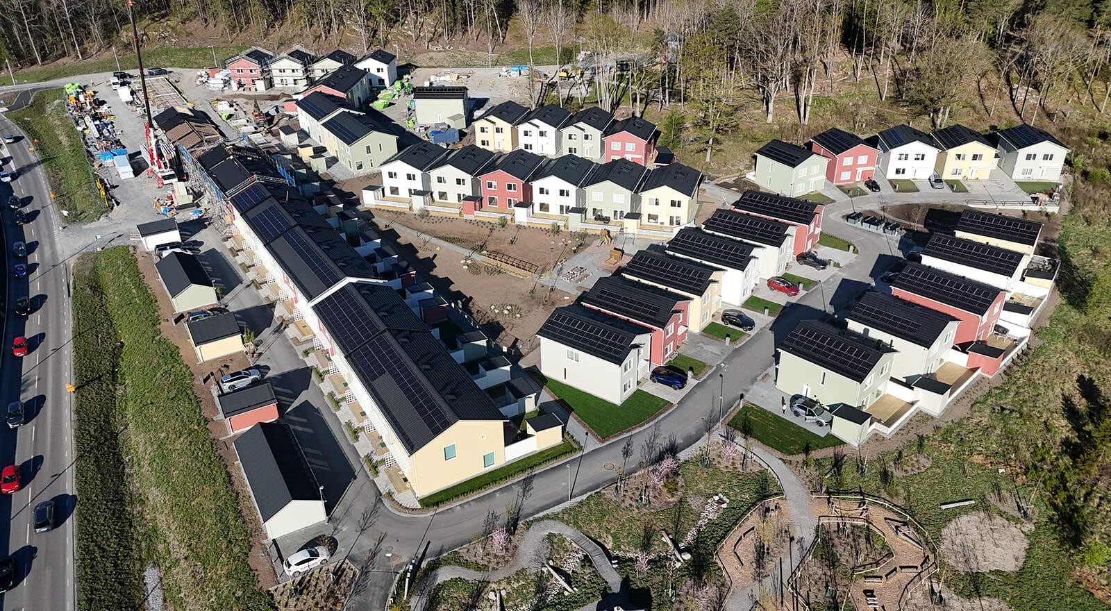 Flygvy över ett nybyggt radhusområde med flera längor, asfalterade interna gator och solceller på nästan alla tak.