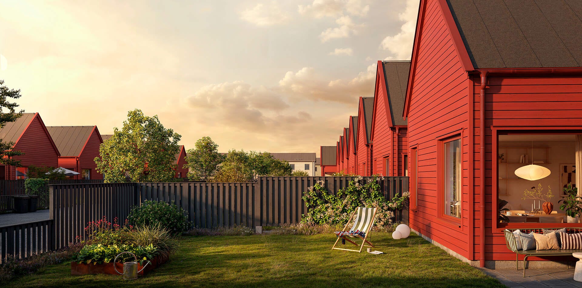 Trädgården blir en plats för hela familjen att koppla av (visualisering) Visualisering - Nyproduktion Linköping – Radhus med röda fasader och trädgård i kvällsljus, med gräsmatta, staket, växter och sittplats utanför.