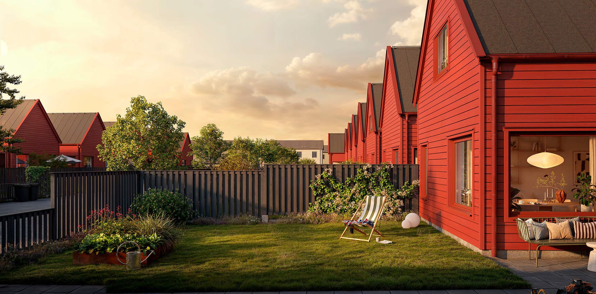 Visualisering - Nyproduktion Linköping – Radhus med röda fasader och trädgård i kvällsljus, med gräsmatta, staket, växter och sittplats utanför.